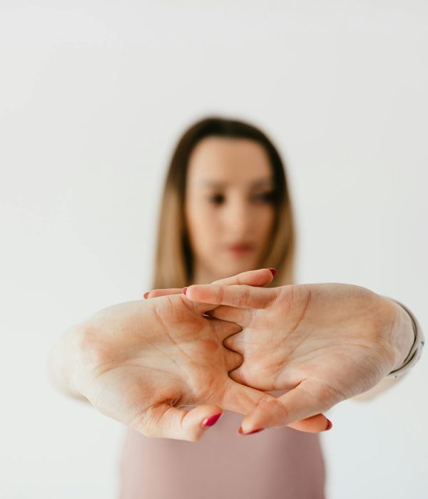Woman performing a gentle stretching yoga pose in a dark, minimalist studio.